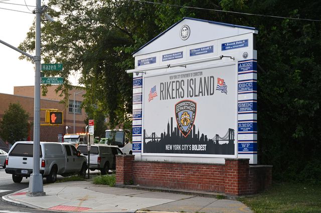 A large sign reading "Rikers Island" near the roadway entrance to the jail.